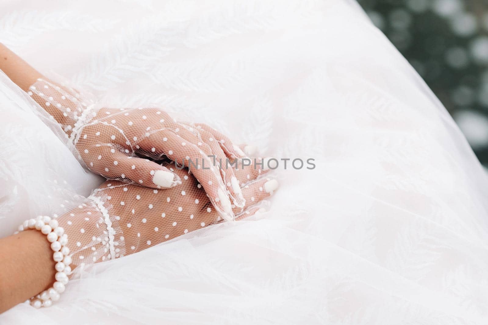 Close-up of the bride's hands in white transparent gloves near a waterfall in the Park.A model in a wedding dress and mesh gloves in a nature Park.Belarus.
