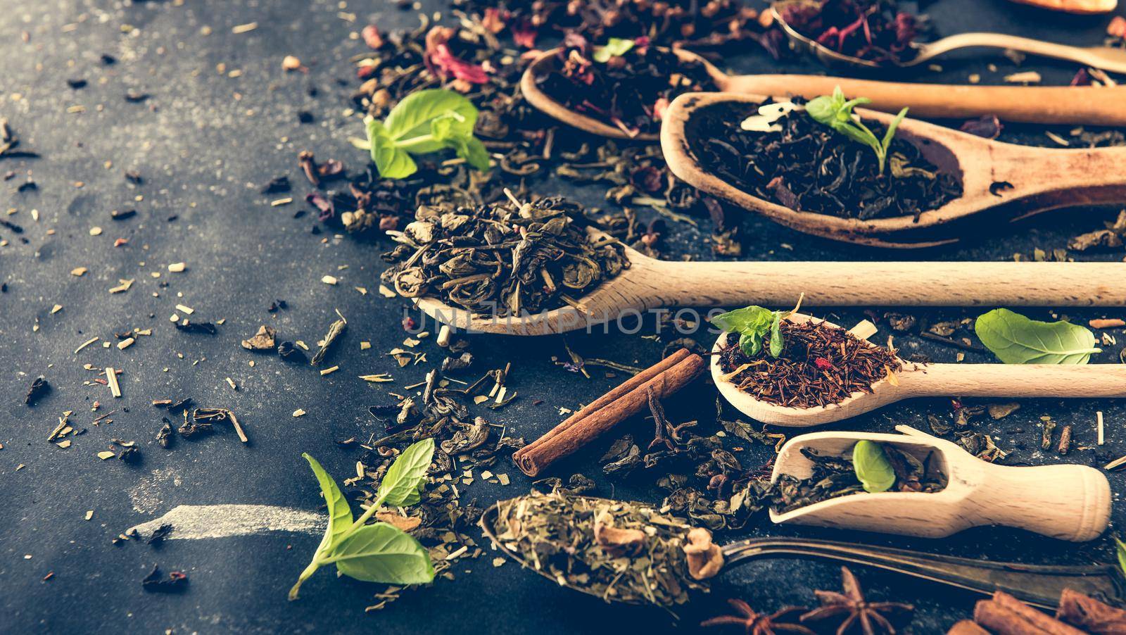 Virious kinds of tea in wooden spoons on black table