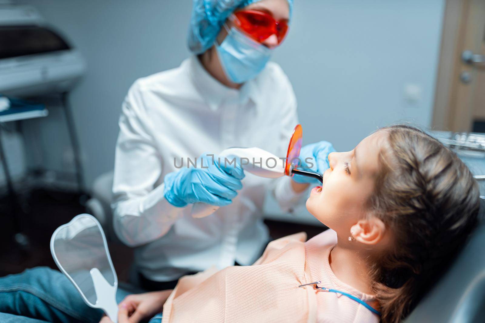 woman dentist providing tooth restoration and filling with curing polymerization UV lamp for her little patient