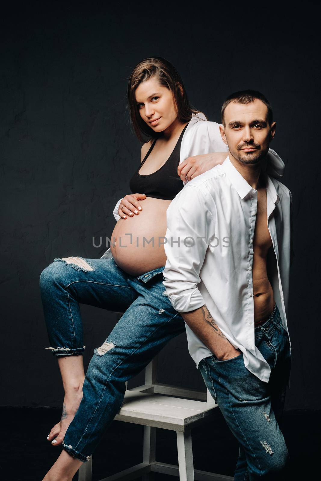 a pregnant woman and a man in a white shirt and jeans in a studio on a black background by Lobachad