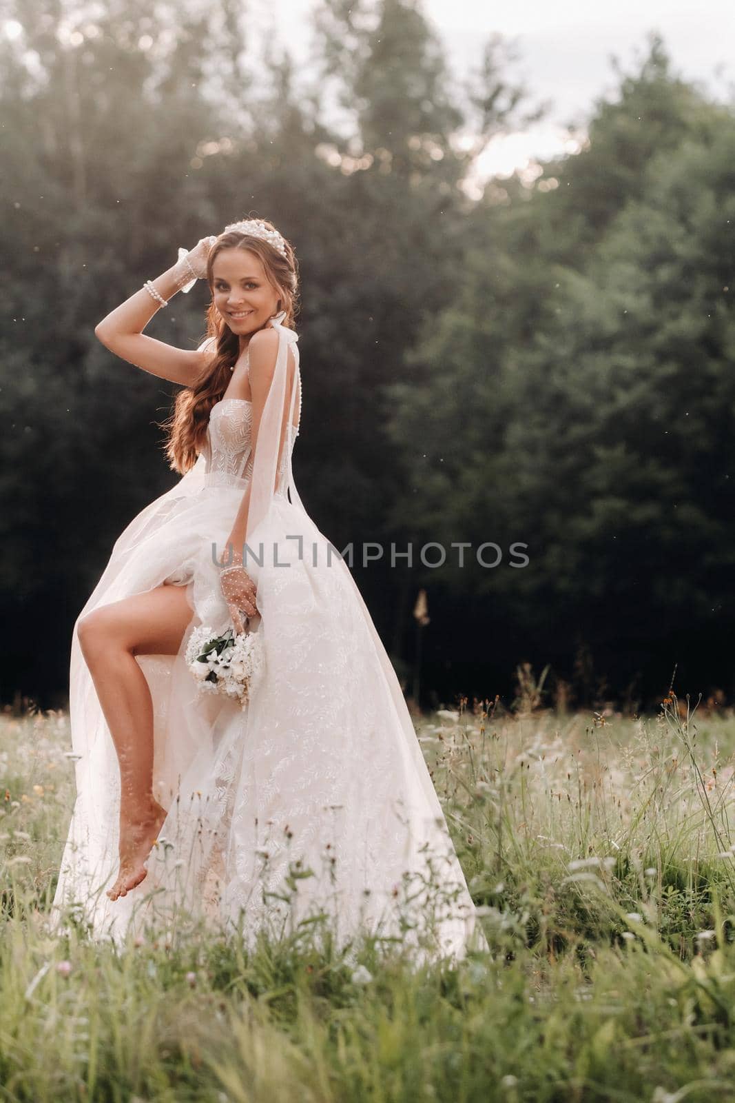 On the wedding day, an Elegant bride in a white long dress and gloves with a bouquet in her hands stands in a clearing enjoying nature. Belarus. by Lobachad