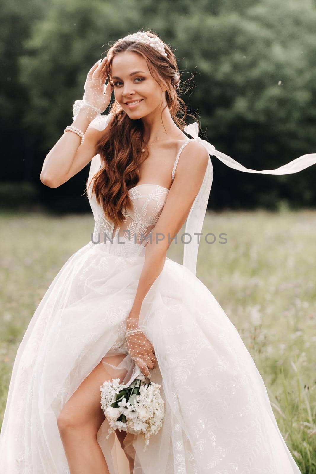 On the wedding day, an Elegant bride in a white long dress and gloves with a bouquet in her hands stands in a clearing enjoying nature. Belarus. by Lobachad