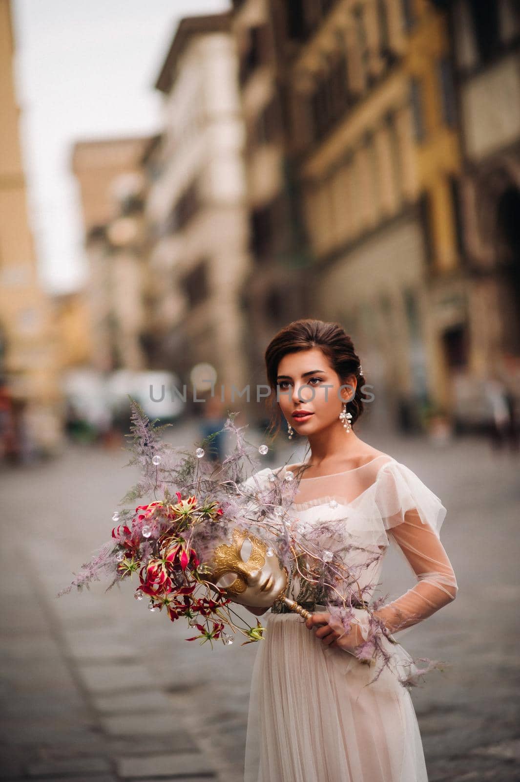 the girl-bride is with beautiful flower pattern as a mask in Florence, stylish bride in a wedding dress standing with a mask in the Old town of Florence. Model girl in Florence by Lobachad