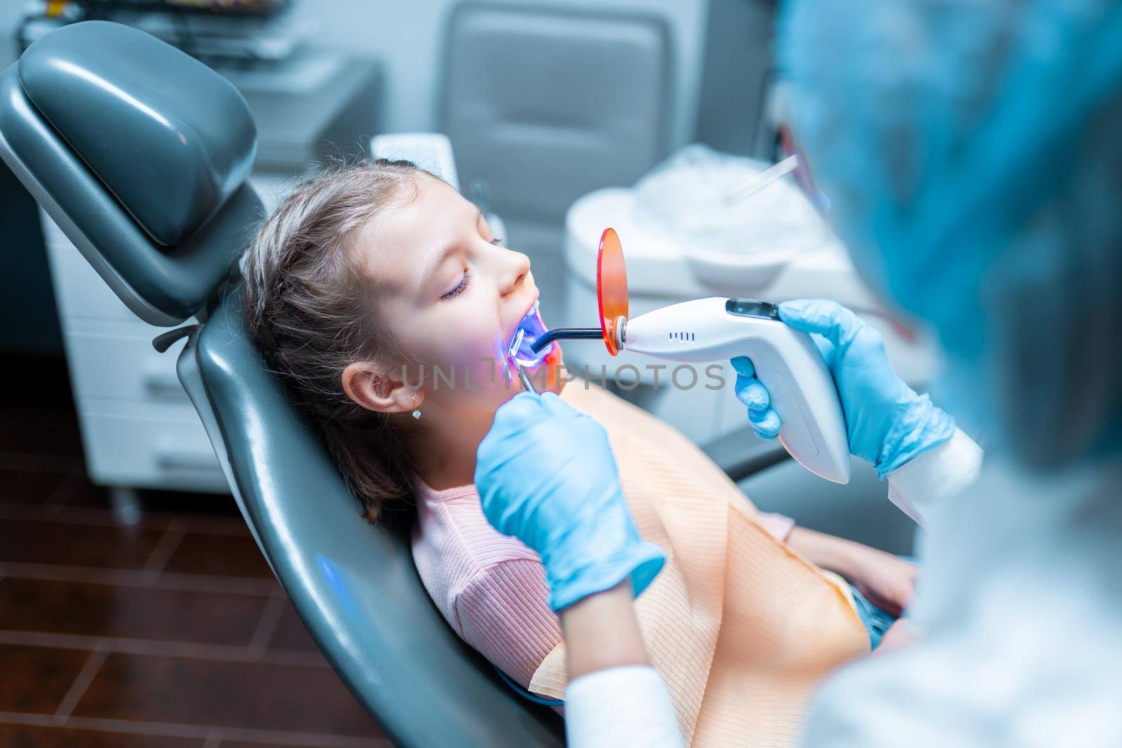 Female dentist providing tooth restoration and filling with curing polymerization UV lamp for her little girl patient