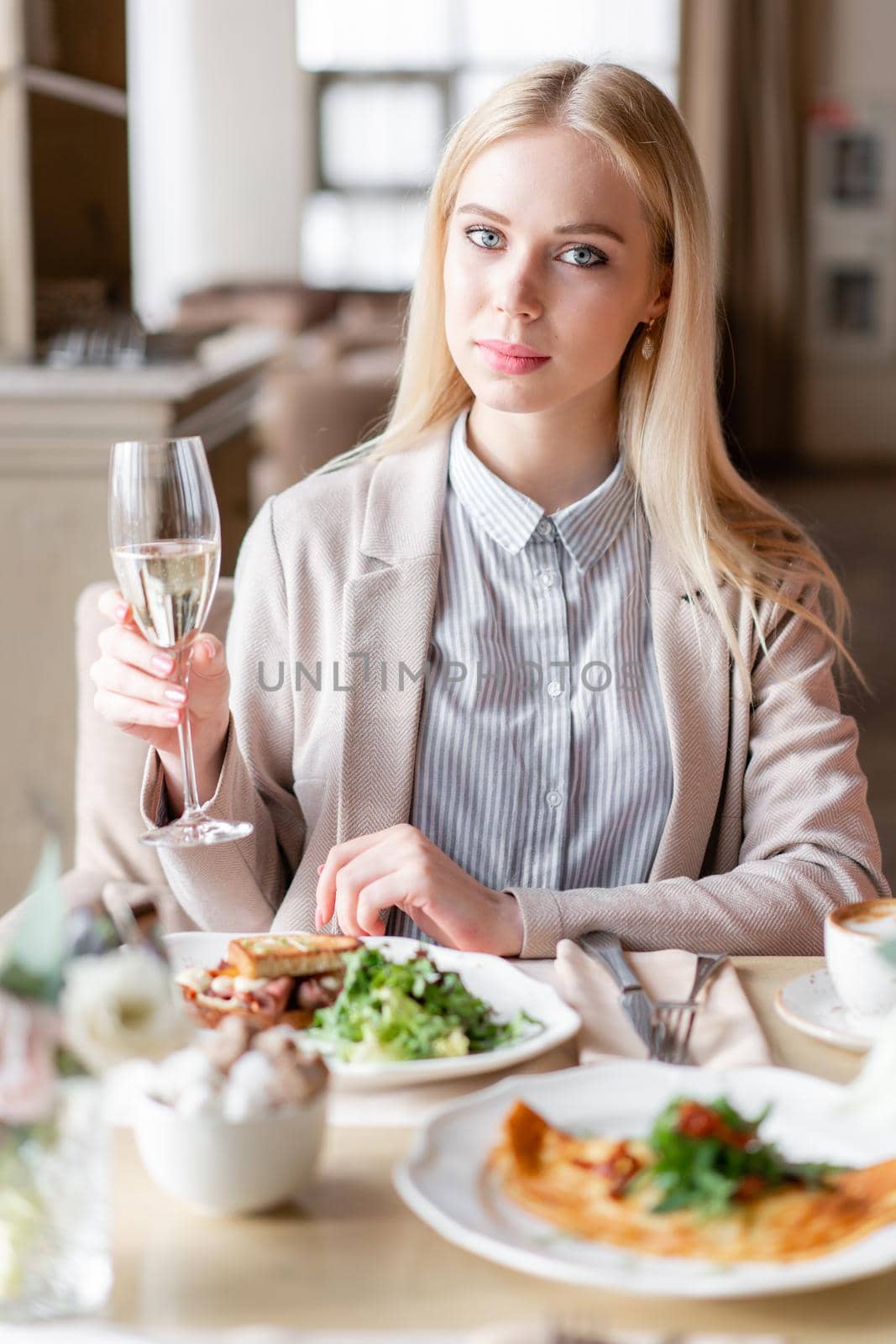 Portrait of a beautiful young elegant blonde woman in the cafe with a glass of champagne