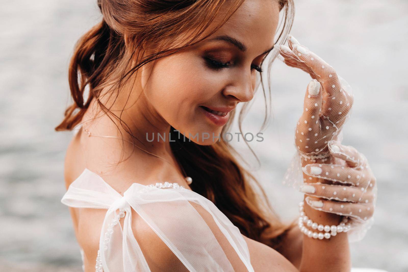 An elegant bride in a white dress, gloves and bare feet is sitting near a waterfall in the Park enjoying nature.A model in a wedding dress and gloves at a nature Park.Belarus by Lobachad