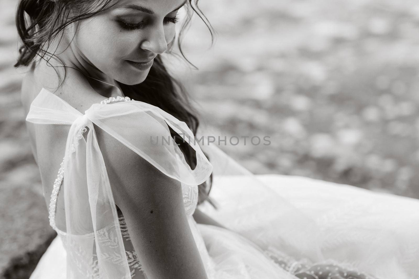 An elegant bride in a white dress and gloves is sitting by the lake in the Park, enjoying nature.A model in a wedding dress and gloves in a nature Park.Belarus.black and white photo.