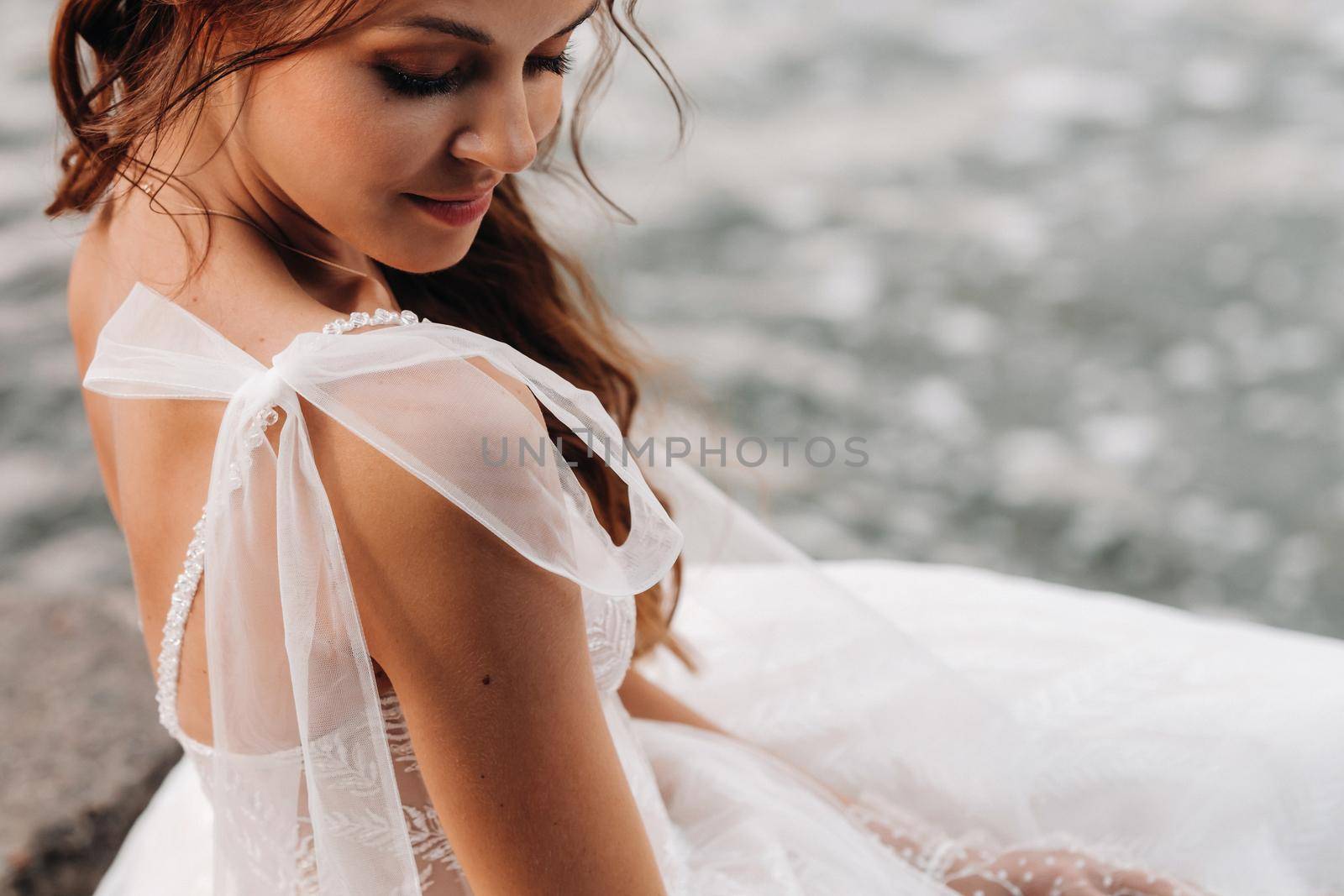 An elegant bride in a white dress and gloves is sitting by the lake in the Park, enjoying nature.A model in a wedding dress and gloves in a nature Park.Belarus