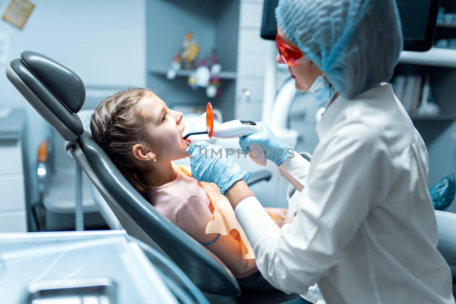 Female dentist providing tooth restoration and filling with curing polymerization UV lamp for little patient