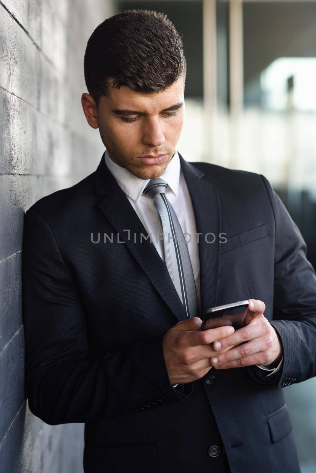 Attractive young businessman on the phone in an office building wearing black suit and tie. Man with blue eyes