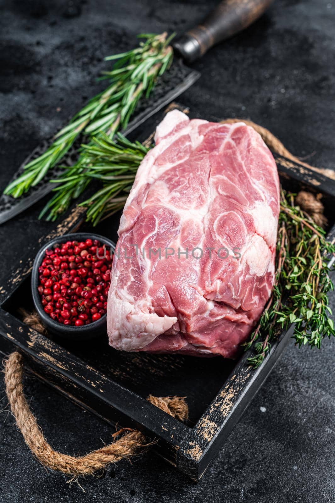 Raw pork neck meat piece for Chop steak in wooden tray with herbs. Black background. Top view by Composter