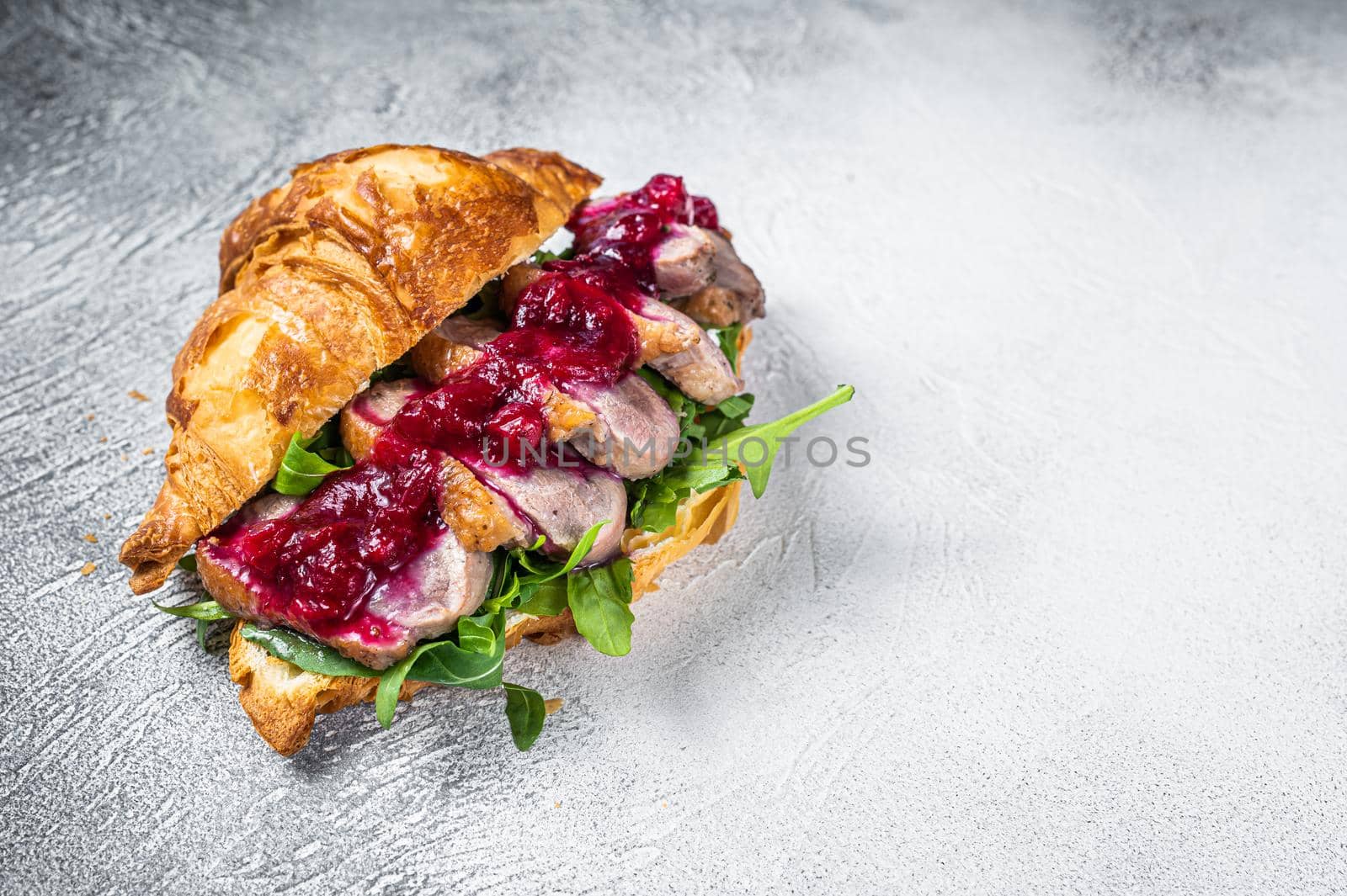 Duck breast Croissant sandwich with steak slices, arugula and sauce. White background. Top View. Copy space.