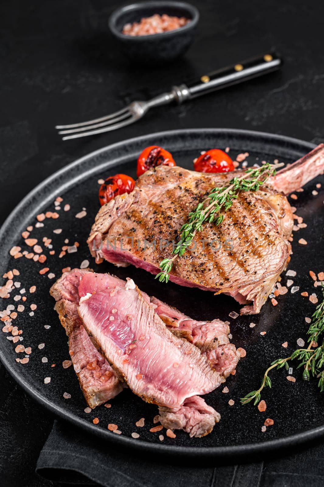 Barbecue sliced rib eye Tomahawk beef (veal) steak on a plate with pink salt. Black background. Top view.