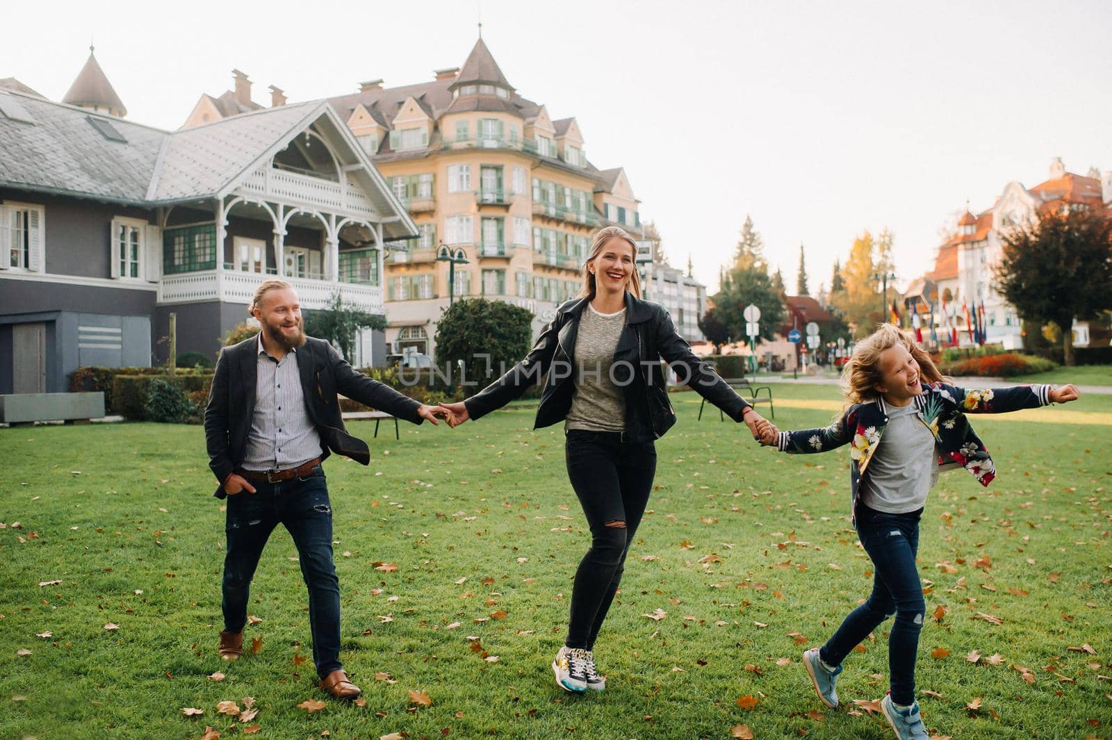 A happy family of three runs through the grass in Austria's old town.A family walks through a small town in Austria.Europe.Velden am werten Zee by Lobachad