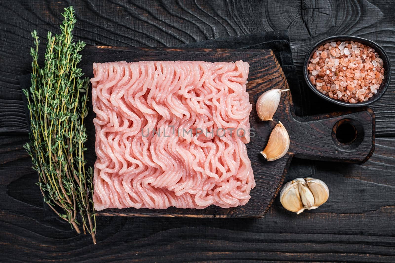 Fresh Raw mince or ground chicken meat on wooden chopping board with thyme. Black wooden background. Top view.