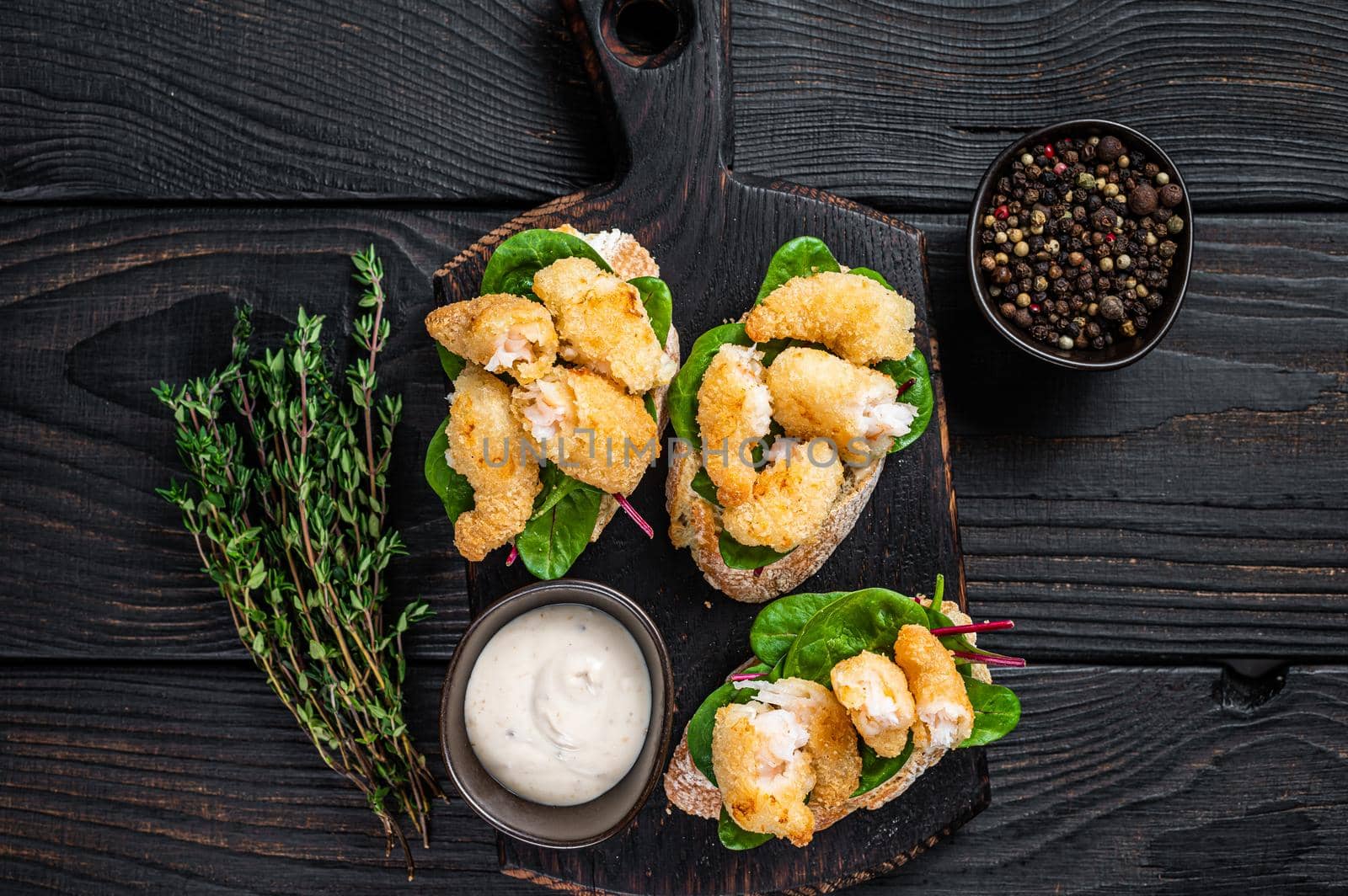 Toasts with Crispy Fried Shrimps Prawns and green salad on a wooden board. Black wooden background. Top view.