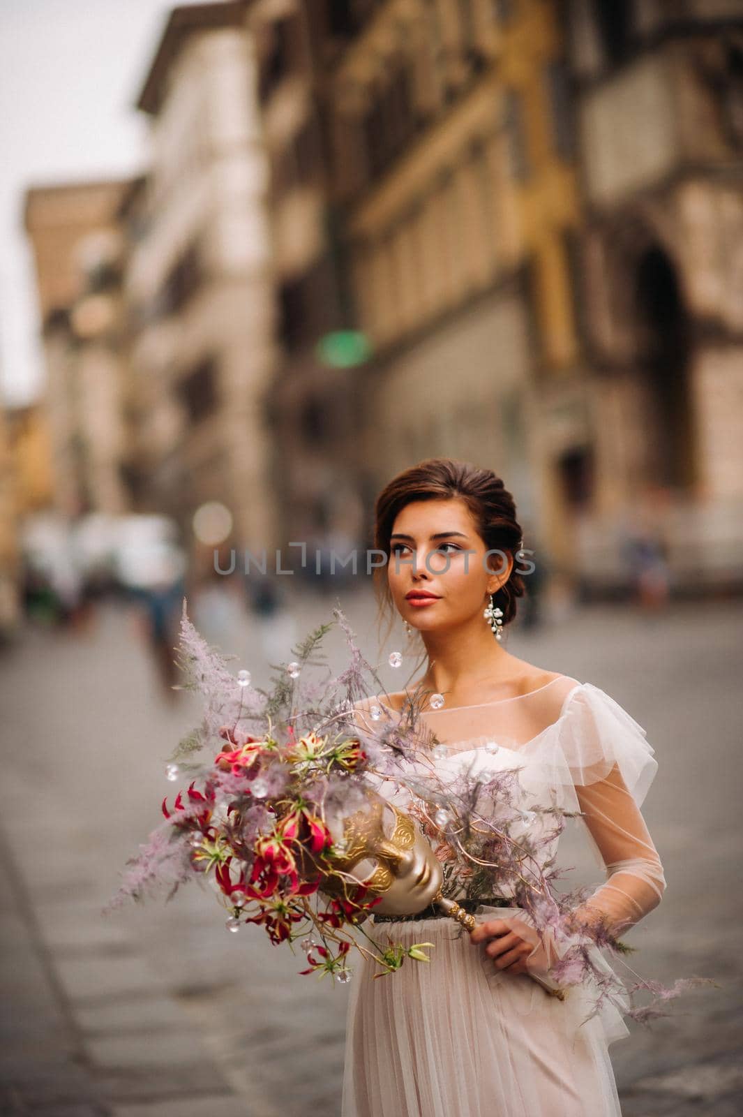 the girl-bride is with beautiful flower pattern as a mask in Florence, stylish bride in a wedding dress standing with a mask in the Old town of Florence. Model girl in Florence.