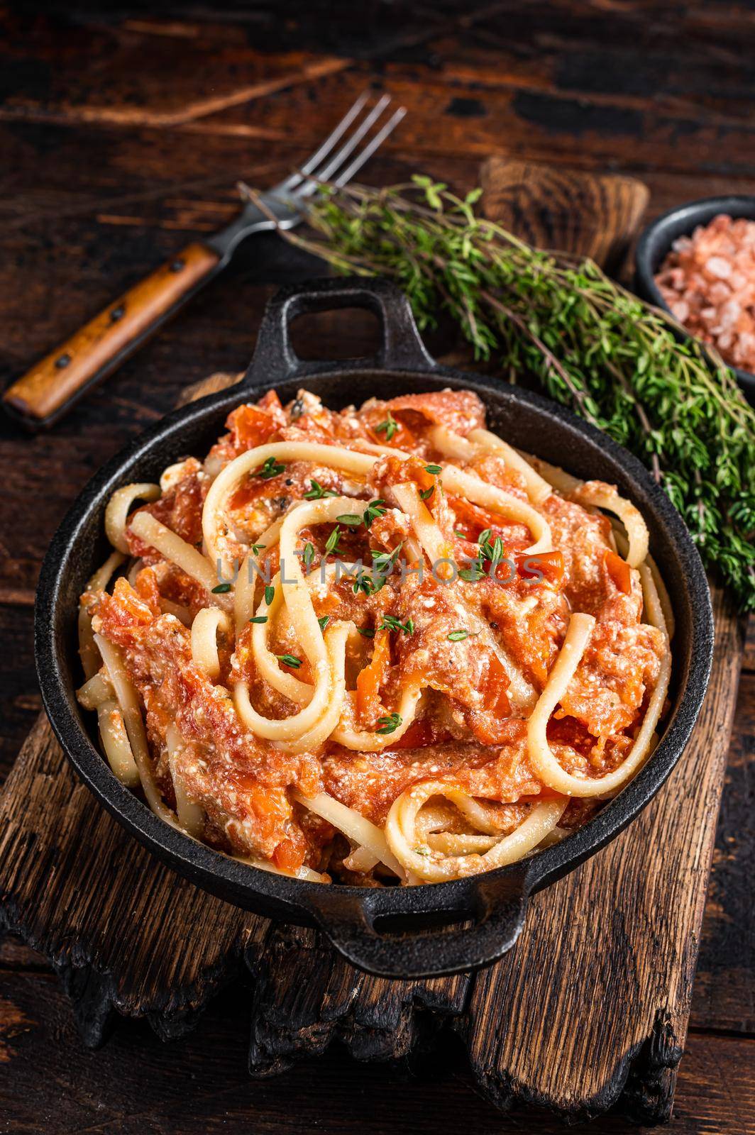 Trendy baked Feta pasta with Oven roasted tomatoes and cheese in a pan. Dark wooden background. Top view by Composter