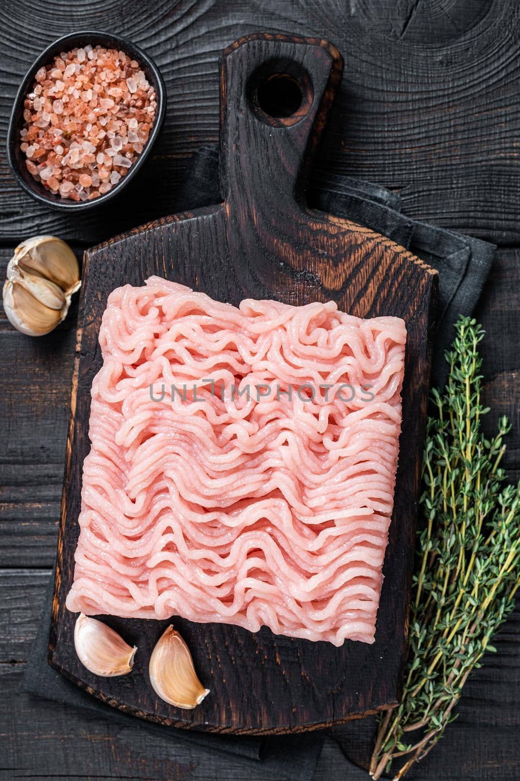 Fresh Raw mince or ground chicken meat on wooden chopping board with thyme. Black wooden background. Top view by Composter