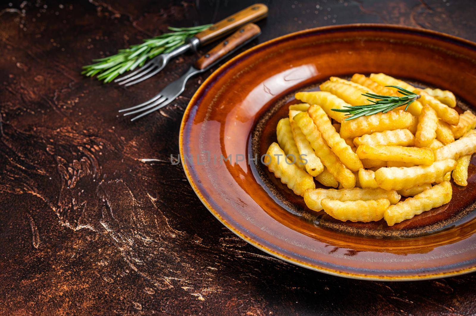 Fried Crinkle French fries potatoes or chips in a rustic plate. Dark background. Top view. Copy space.