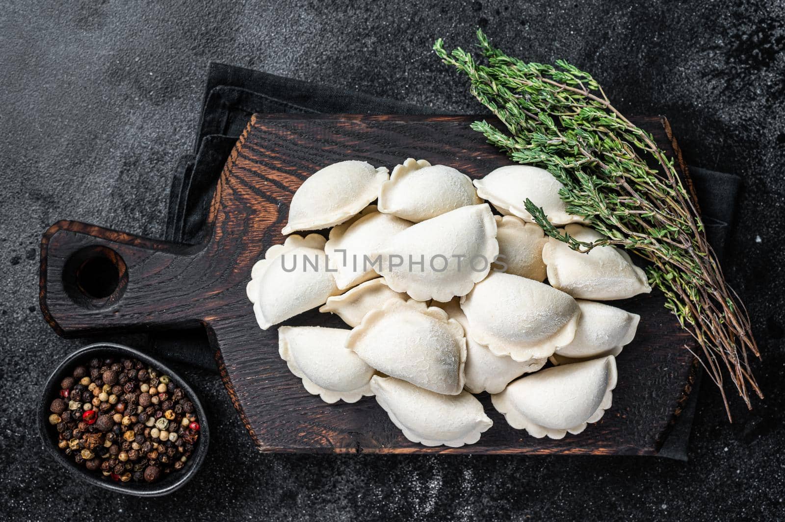 Frozen raw dumplings pierogi with potato on a wooden board. Black background. Top View.