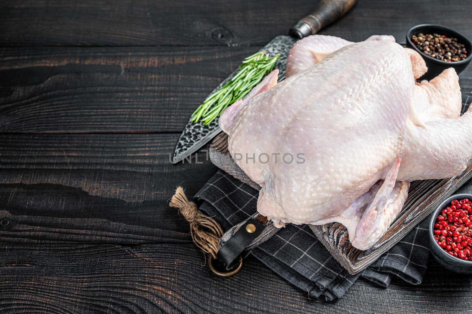 Raw whole chicken, poultry meat on a wooden board with herbs. Black Wooden background. Top view. Copy space by Composter