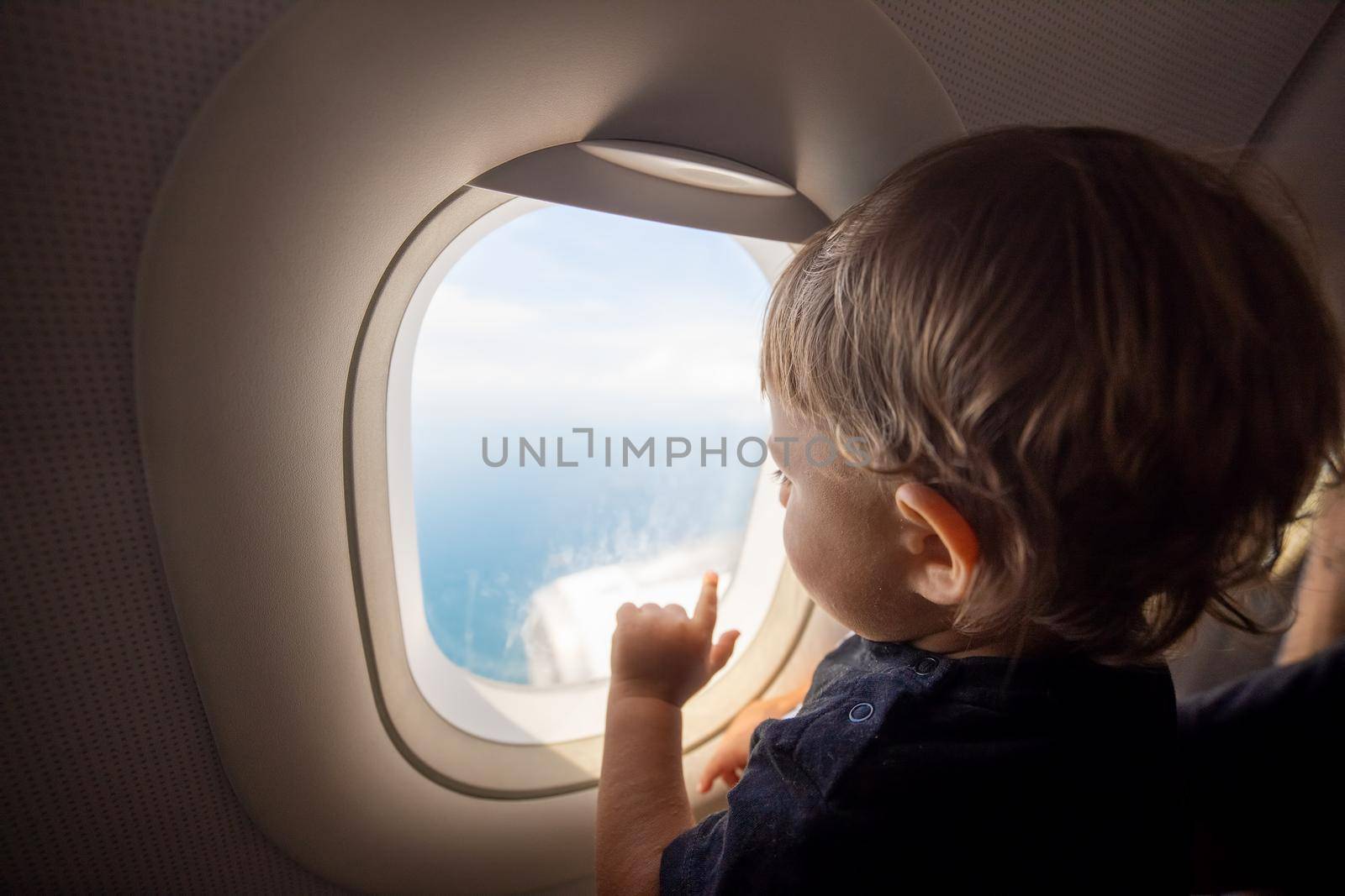 resumption of flights, opening of borders concept. a small child looks at the ocean from the window of a flying plane. first flight. vacation happiness. soft focus