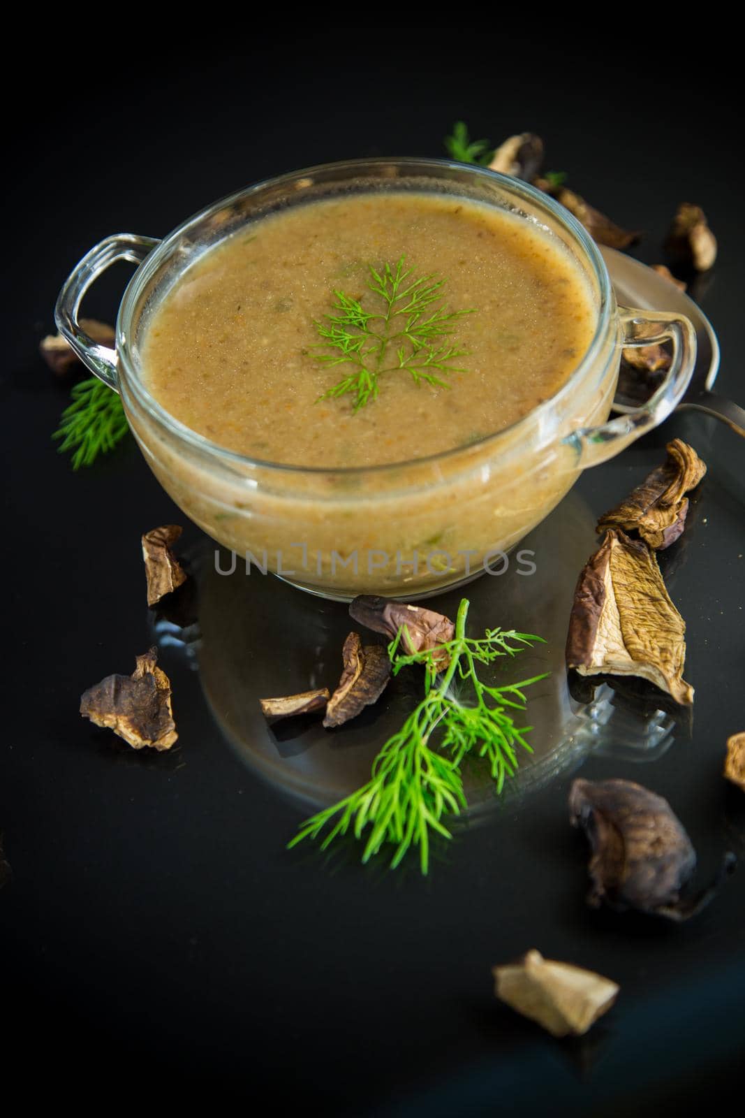 hot homemade vegetable vegetarian soup with dried mushrooms in a glass bowl on black background