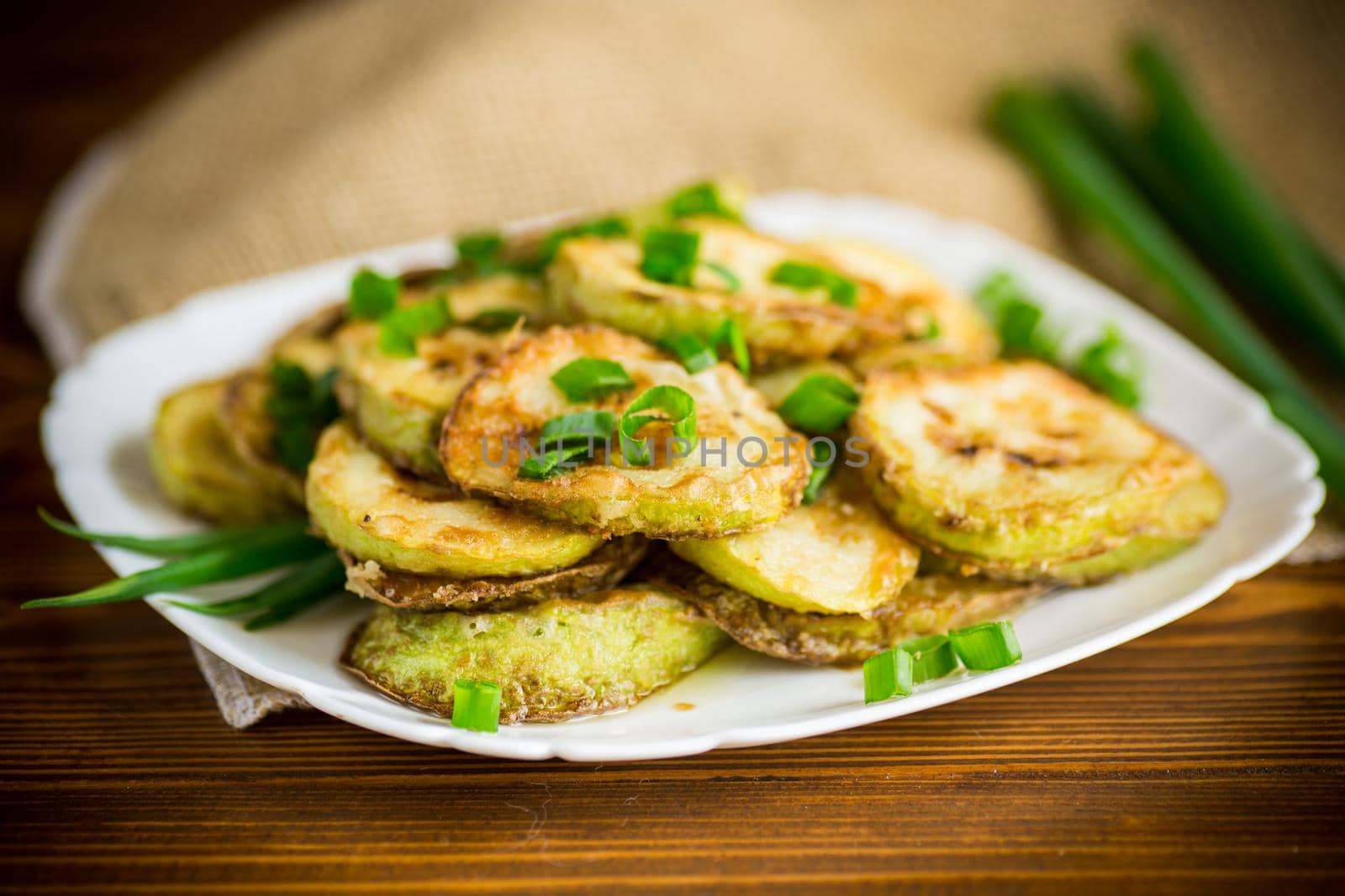 fried zucchini in circles with fresh herbs in a plate on a wooden table