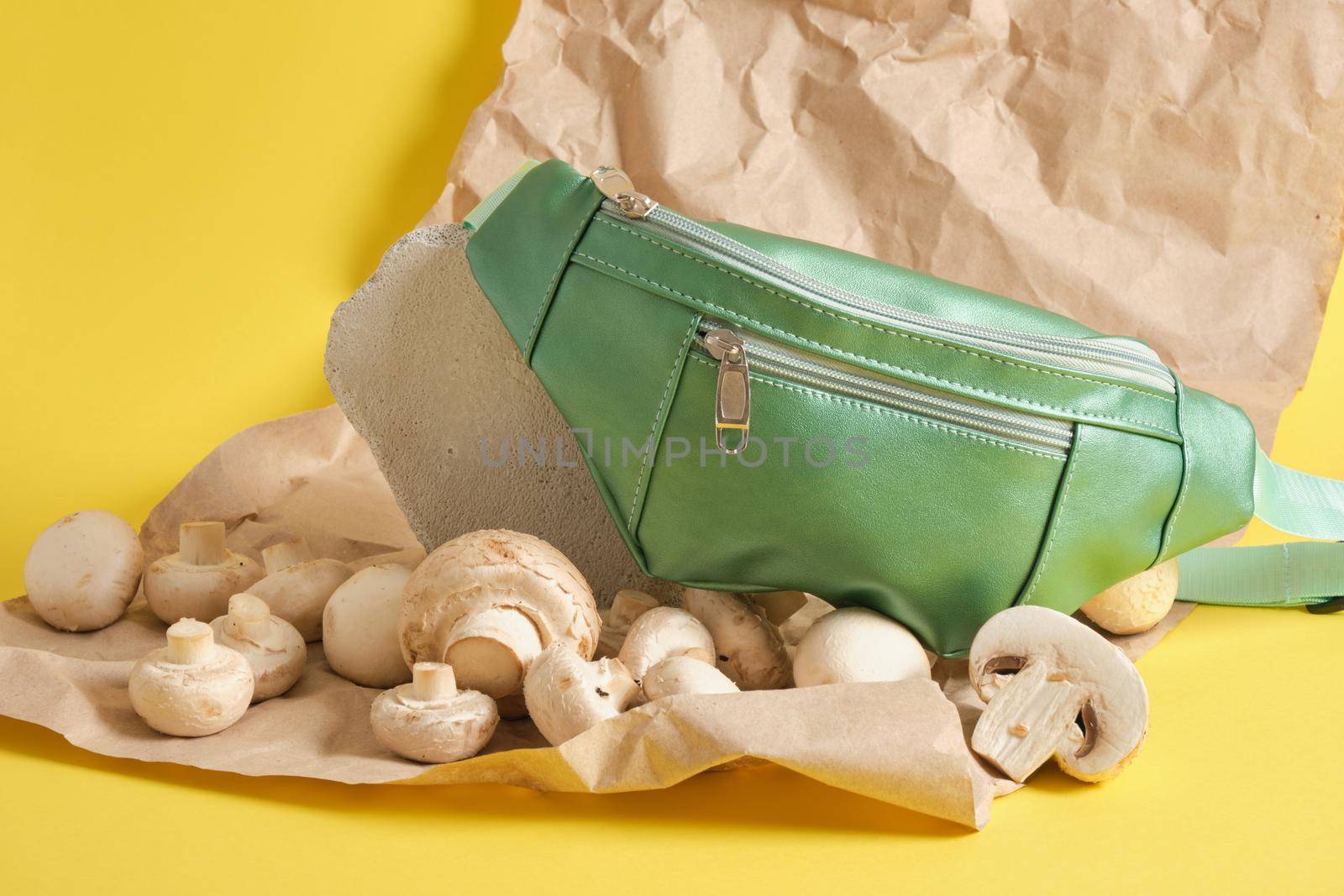 green belt bag made of ecoleather and champignons on yellow background, vegan leather from mushroom mycelium concept, environmental protection and animals