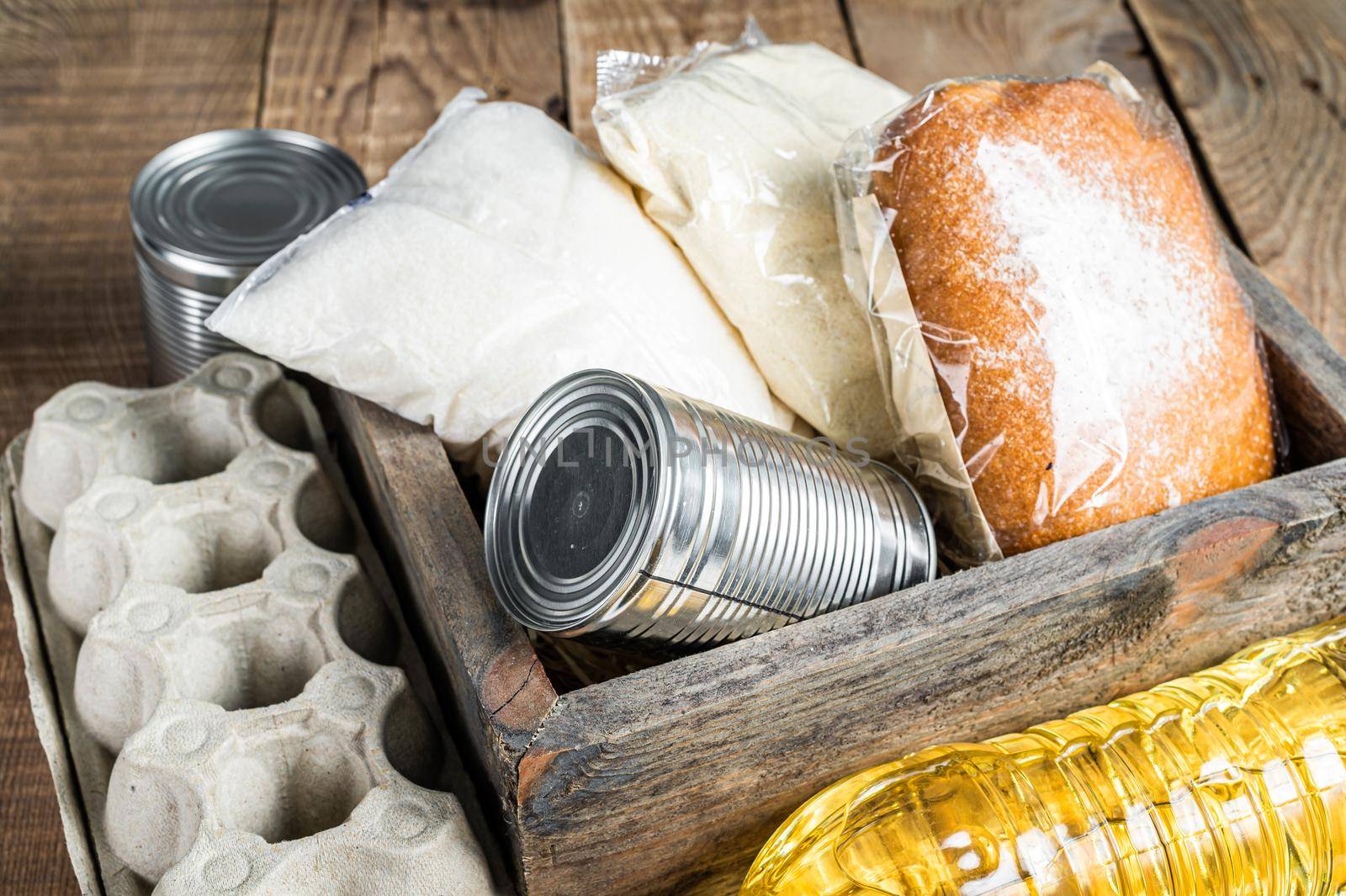 Wooden box with Donation food, quarantine help concept. Oil, canned food, pasta, bread, sugar, egg. Wooden background. Top view by Composter