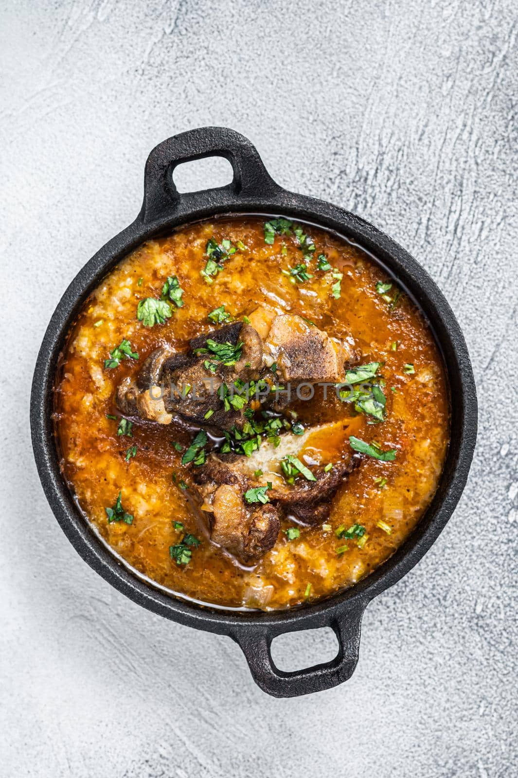 Kharcho soup with beef meat, rice, tomatoes and spices in a pan. White background. Top view.