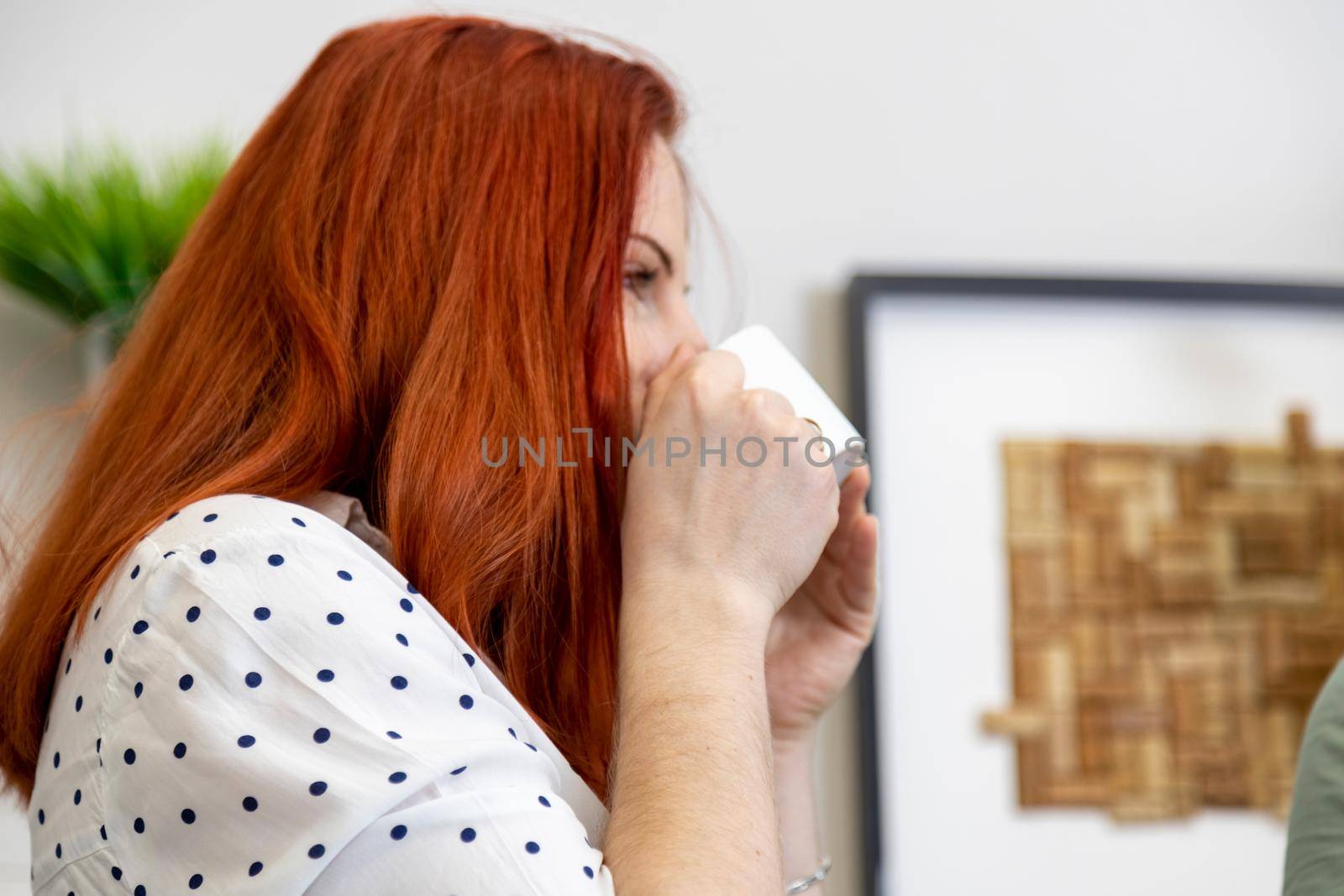 portrait of red-haired woman enjoys drinking coffee from a white cup in cafe. side view close up