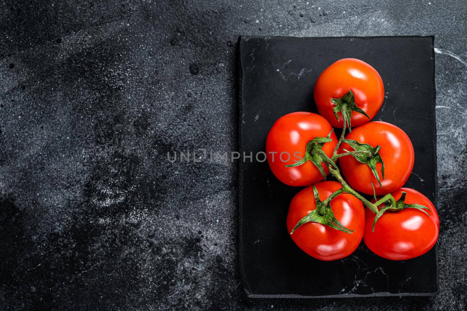 Branch of Red cherry tomatoes on marble board. Black background. Top view. Copy space by Composter