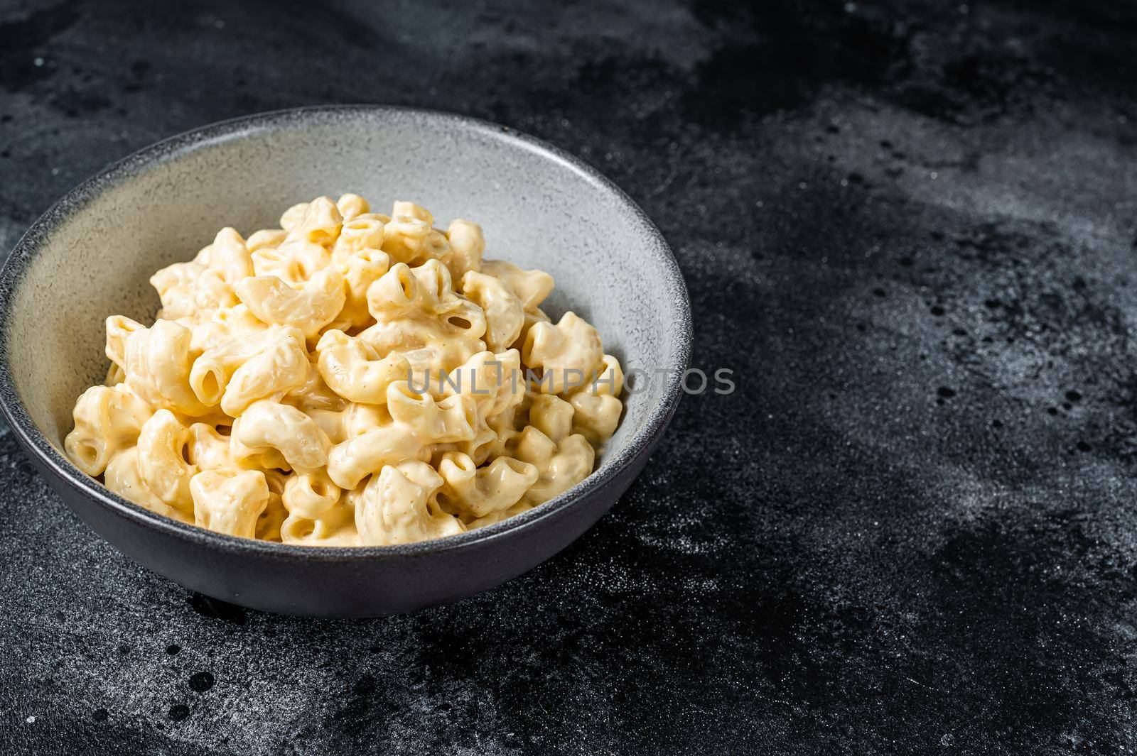 Mac and cheese american macaroni pasta with cheesy Cheddar sauce. Black background. Top view. Copy space by Composter
