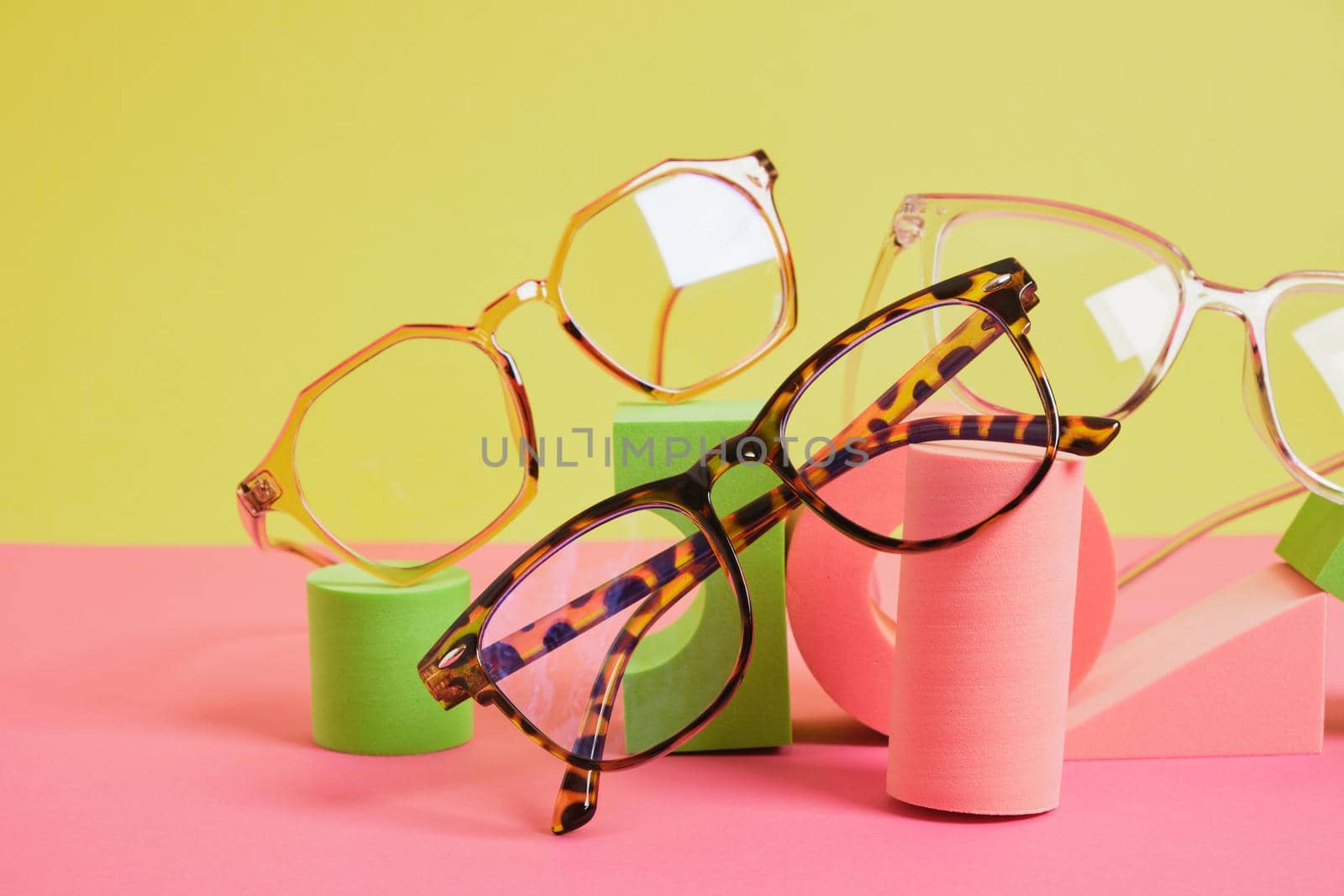 trendy eye glasses on geometric pink podiums, colorful background, copy space by natashko