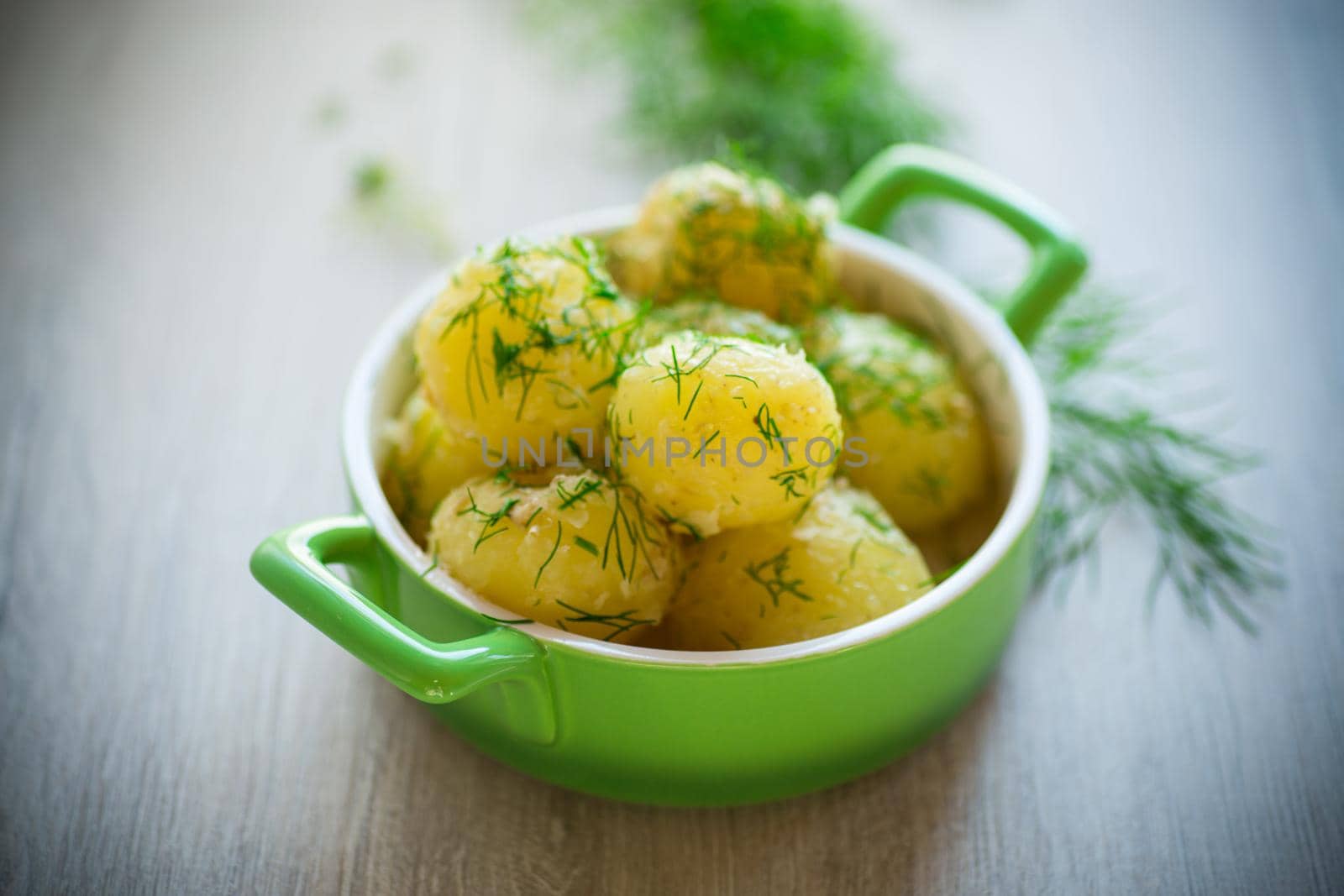 boiled early potatoes with butter and fresh dill in a bowl on a wooden table