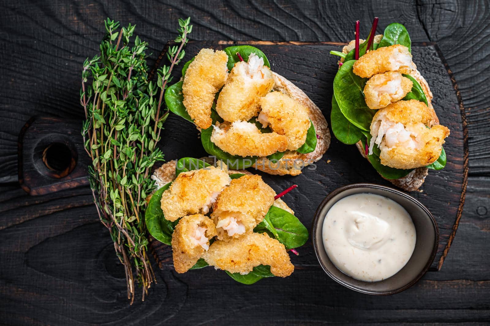 Toasts with Crispy Fried Shrimps Prawns and green salad on a wooden board. Black wooden background. Top view.