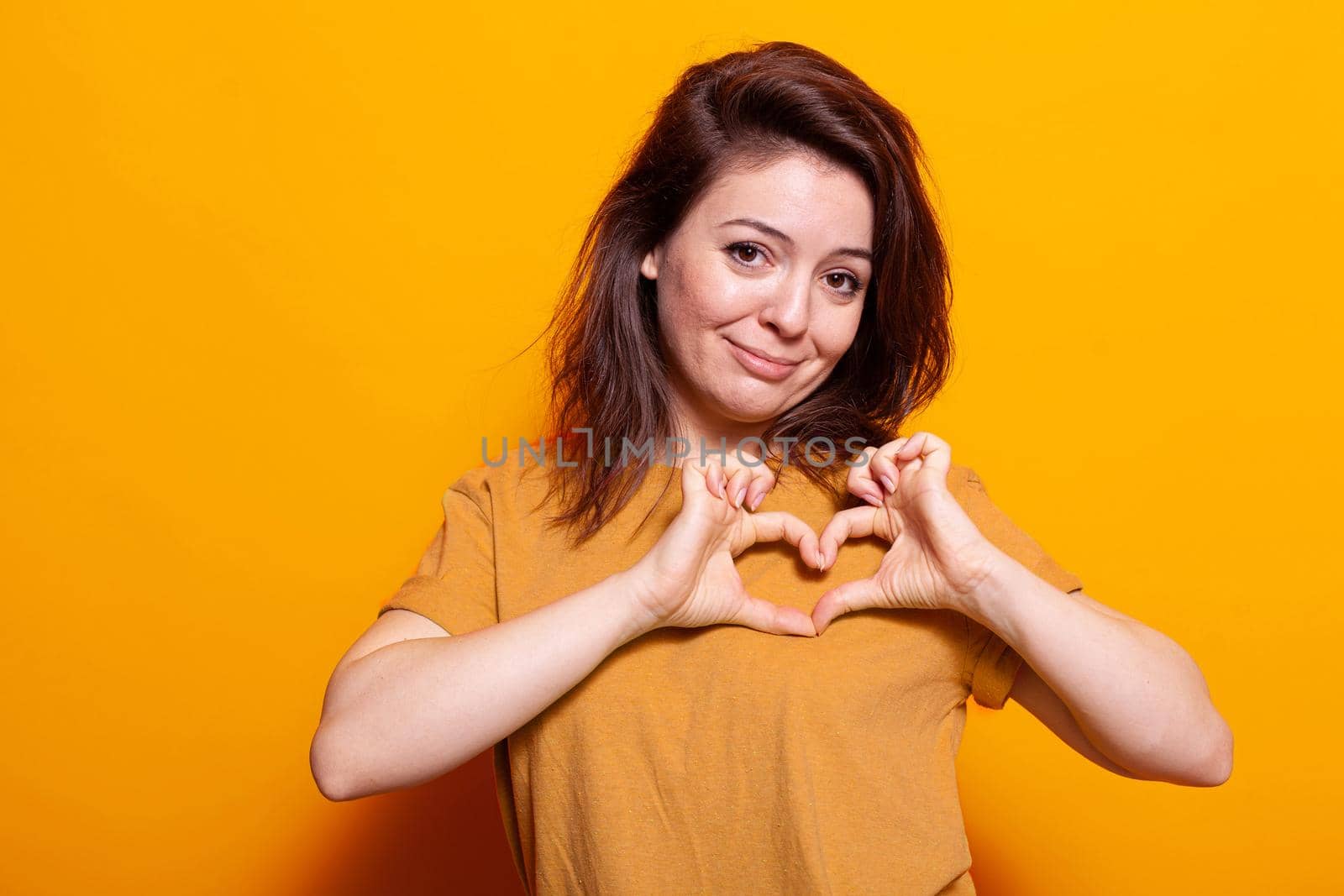 Caucasian woman showing heart shape with fingers at camera by DCStudio