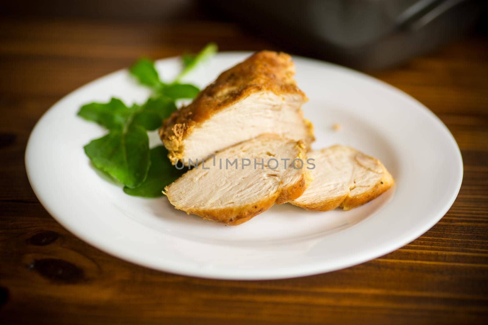 baked chicken fillet pieces with spices and herbs, in a plate on a wooden table