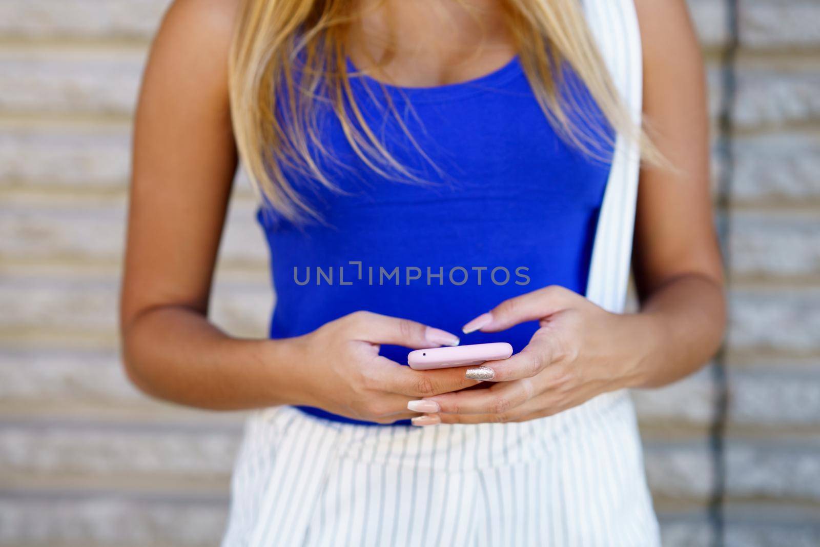 Young female with gel nails using a smartphone outdoors.
