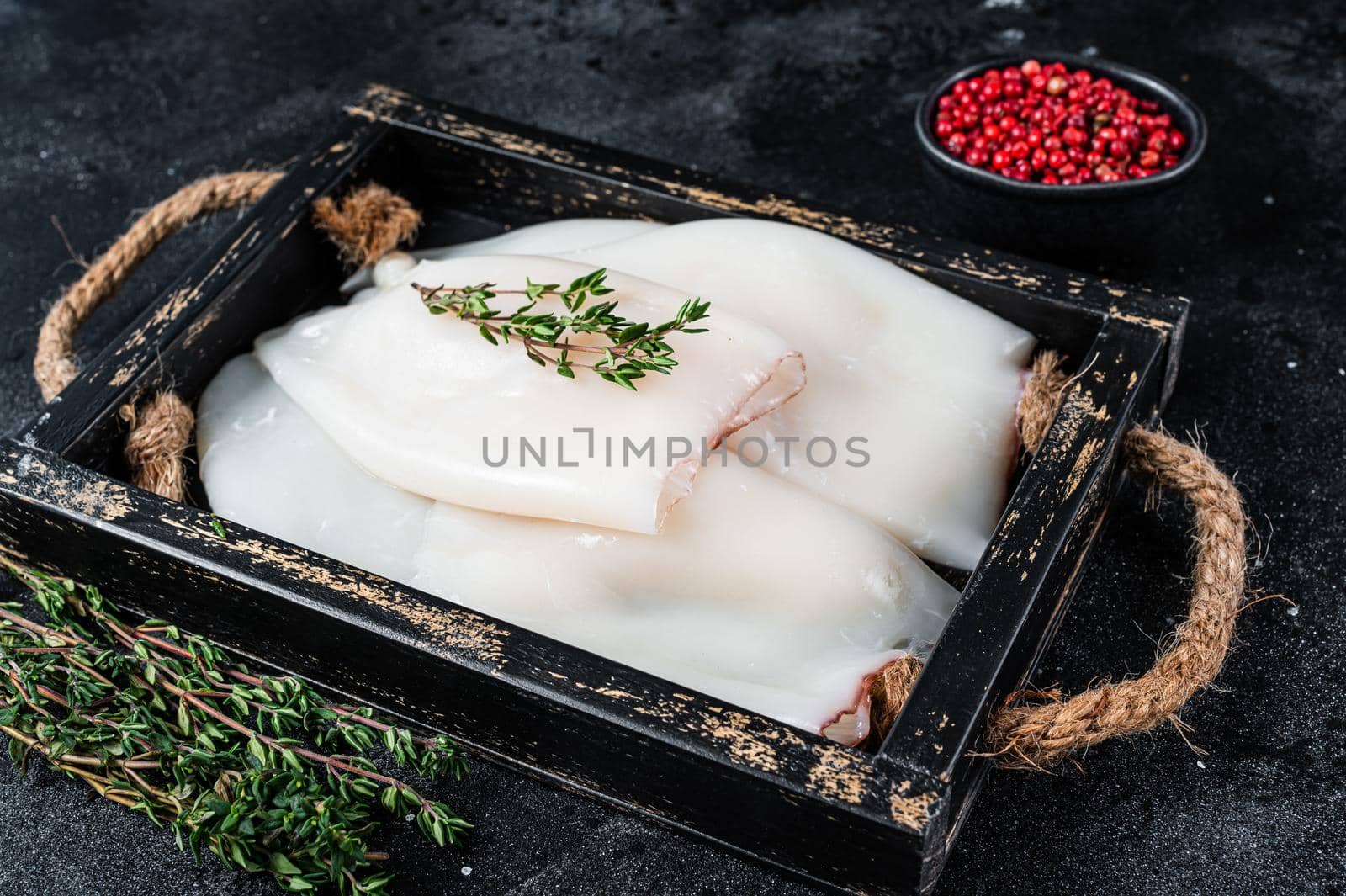Raw white Squid or Calamari in a wooden tray with herbs. Black background. Top view by Composter