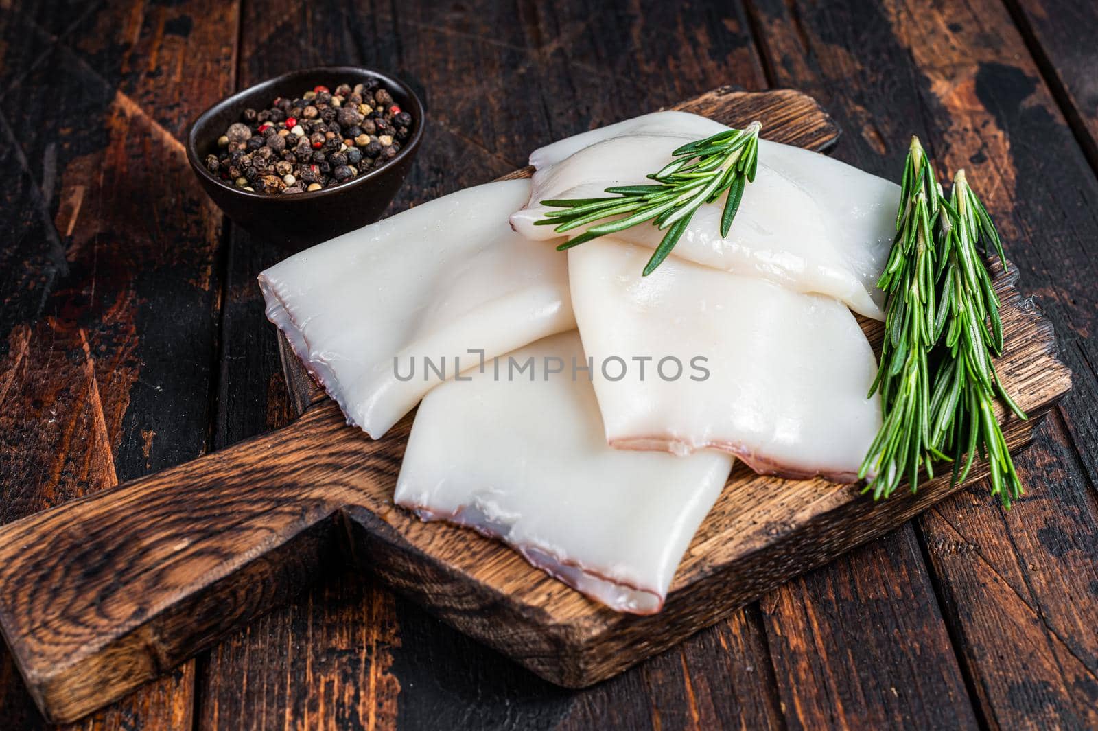 Raw Calamari or Squid on a wooden board with rosemary. Dark wooden background. Top view.