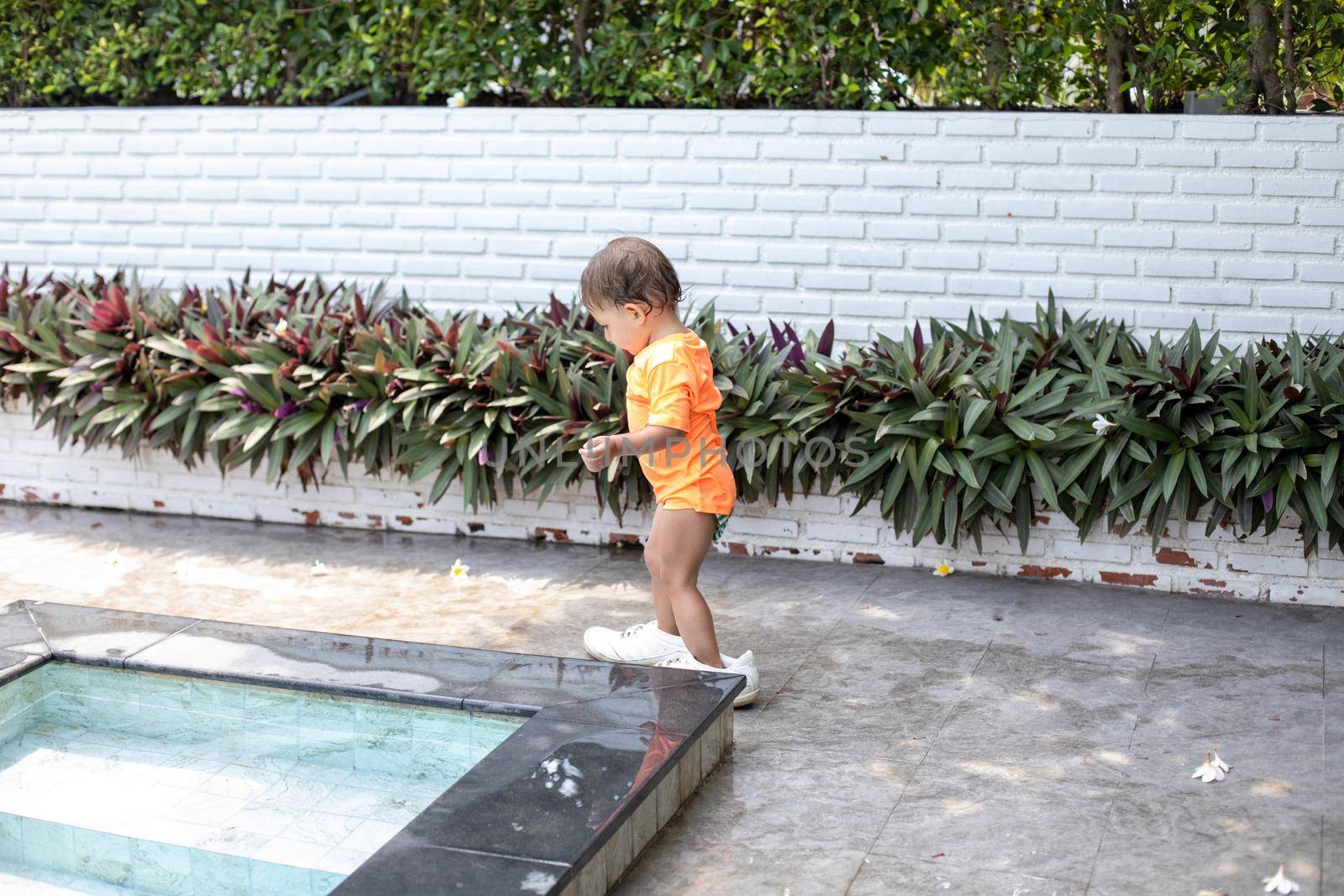 little toddler girl walks in adult shoes by the swimming pool.