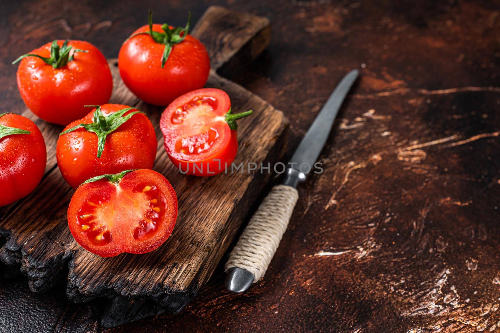Cut Red cherry tomatoes on wooden cutting board. Dark background. Top view. Copy space by Composter