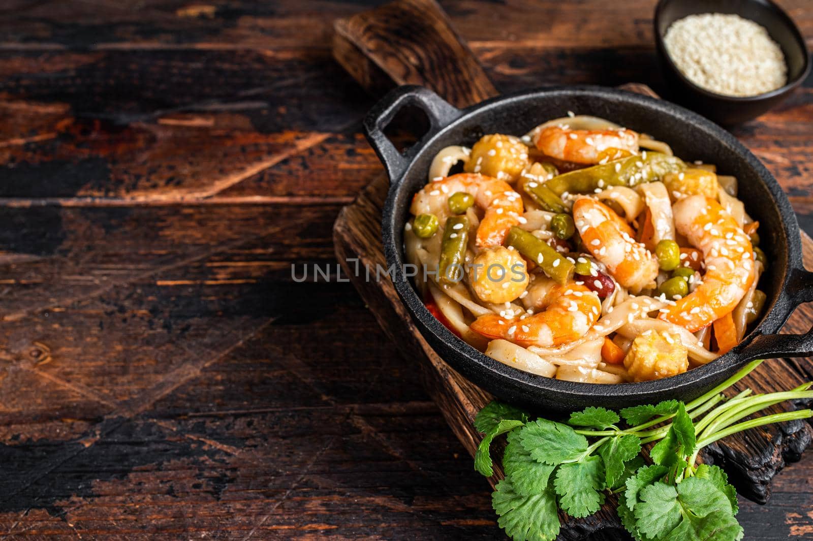 Asian Udon stir-fry noodles with shrimps prawns in a pan. Dark wooden background. Top view. Copy space by Composter