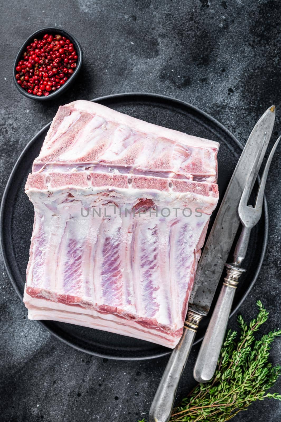 Fresh Raw whole rack of pork loin chops with ribs on a plate with meat fork. Black background. Top view.