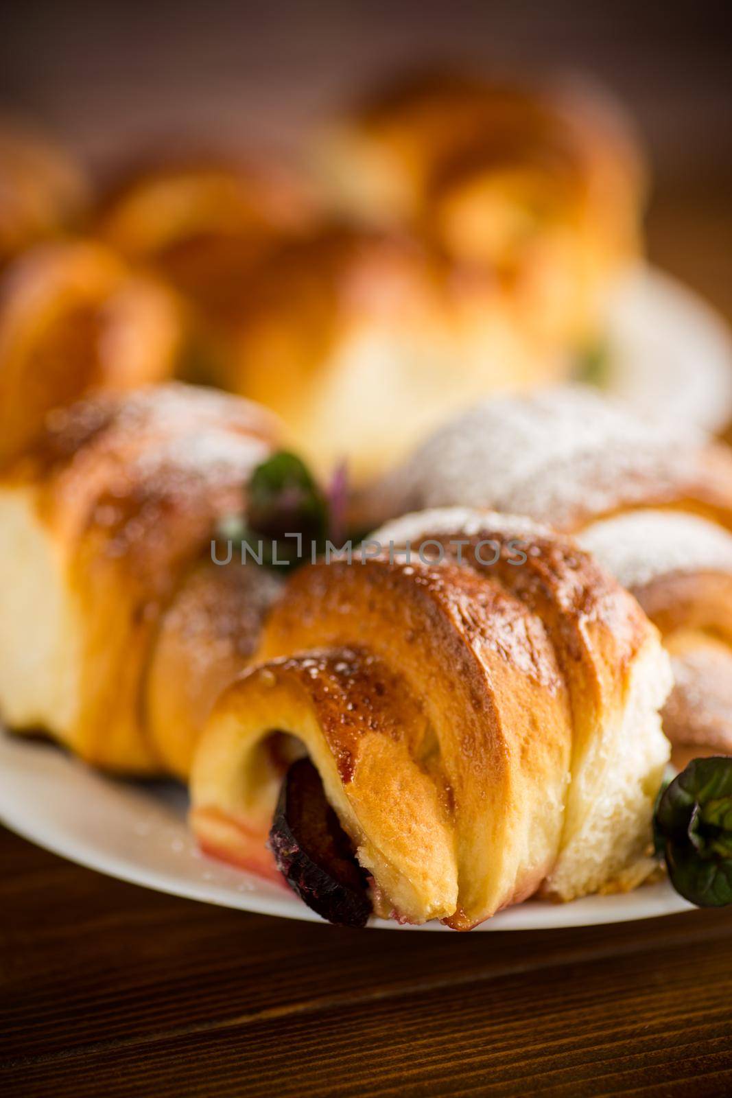 baked sweet homemade buns with plum inside, on a wooden table.