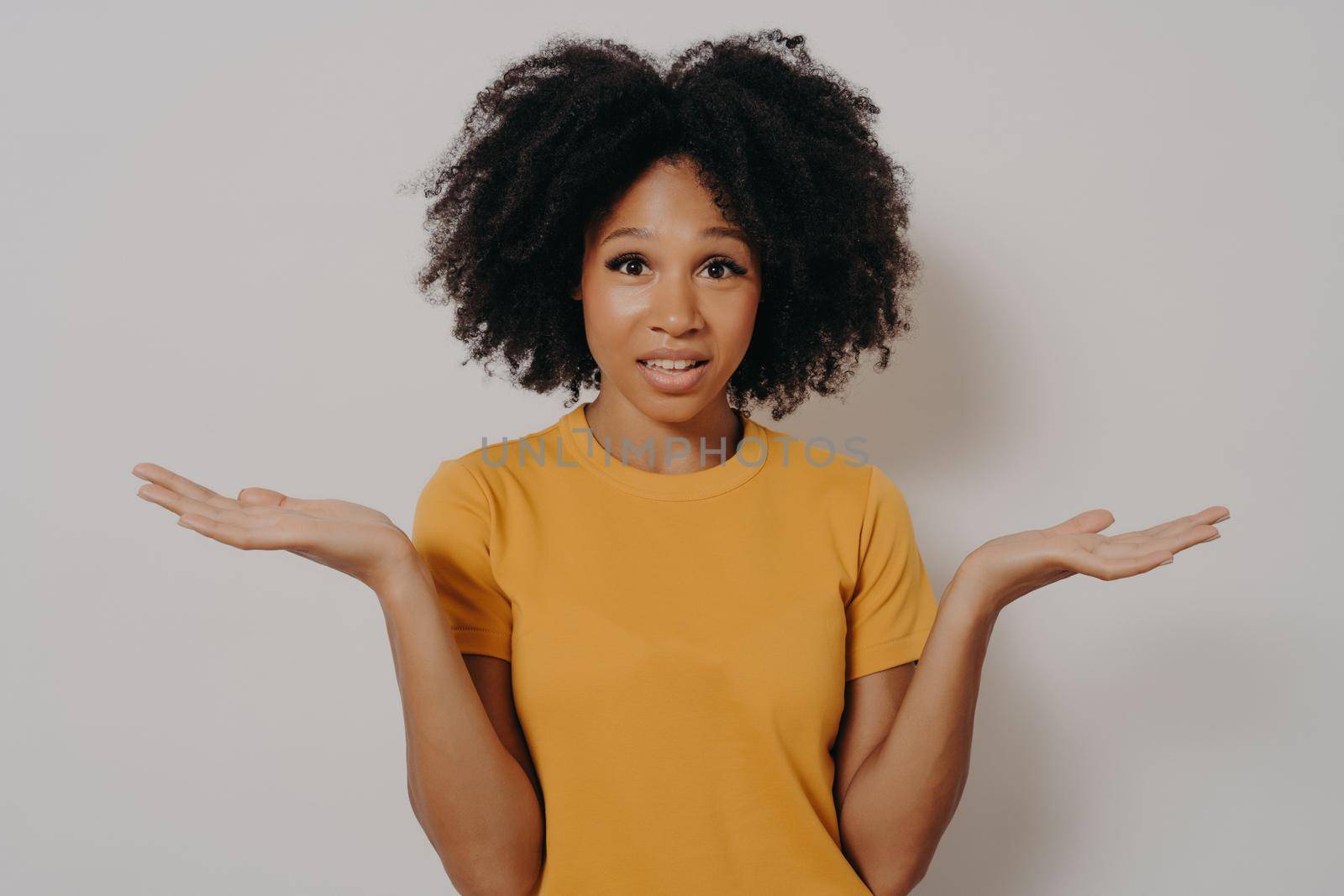 Confused doubtful black woman shrugging with shoulders, feeling baffled while looking at camera by vkstock