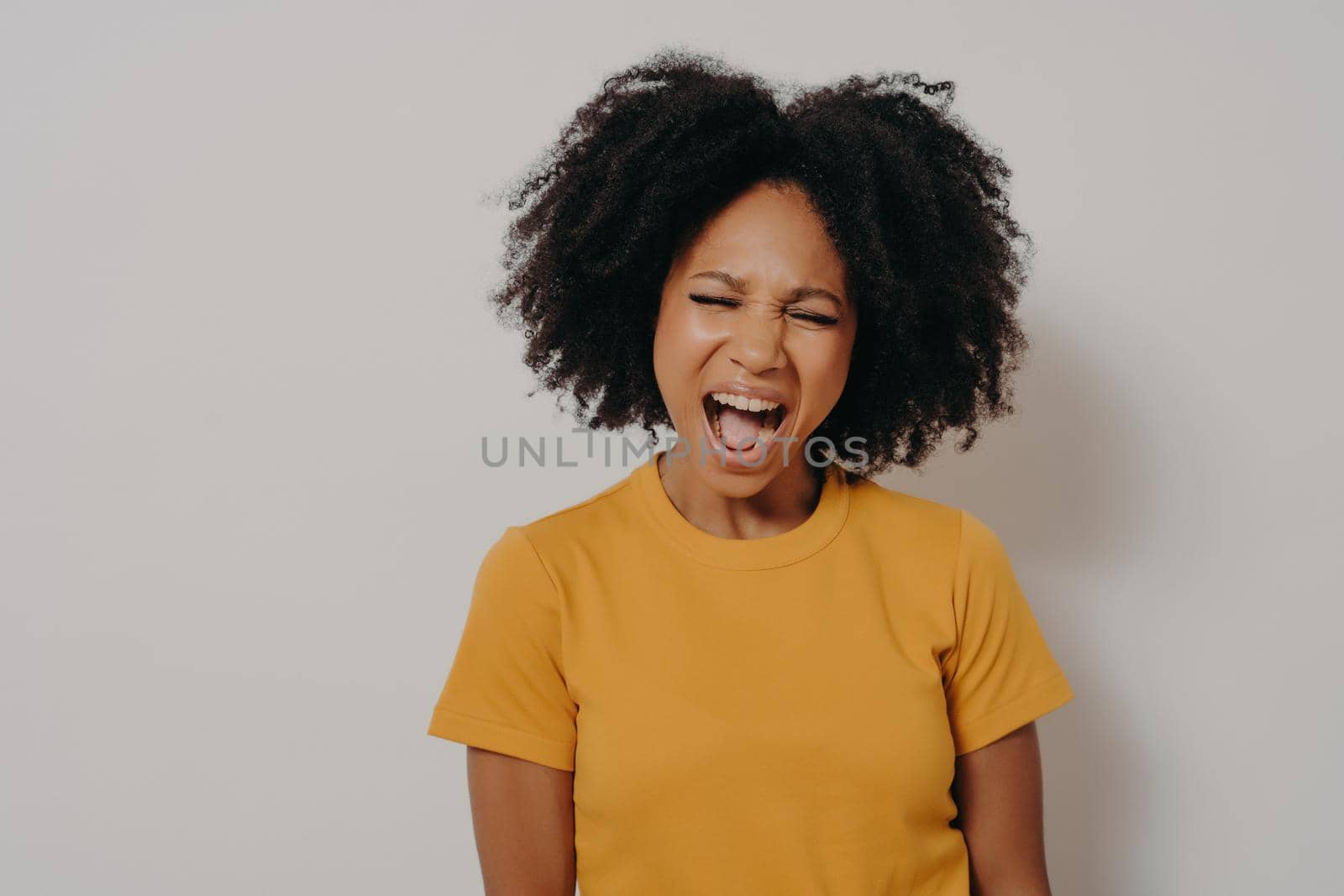 Young beautiful African American woman with curly hair wearing casual yellow tshirt shouting with anger and madness, girl is frustrated and furious. Rage and aggressive concept